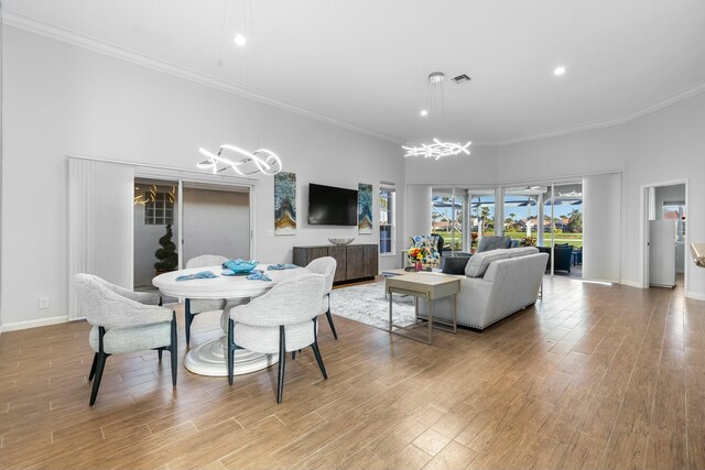 living room featuring a high ceiling, ornamental molding, a notable chandelier, and light hardwood / wood-style flooring