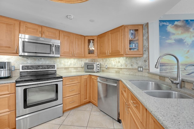 kitchen featuring appliances with stainless steel finishes, sink, light stone counters, light tile patterned floors, and decorative backsplash