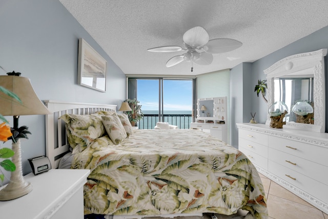 bedroom with access to exterior, light tile patterned floors, a water view, a textured ceiling, and ceiling fan