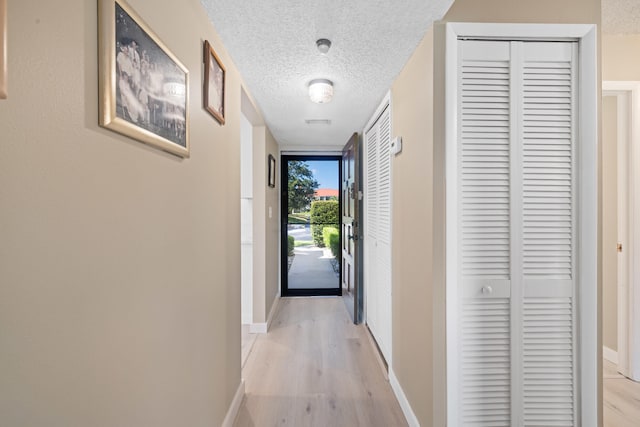 hallway with a textured ceiling and light wood-type flooring