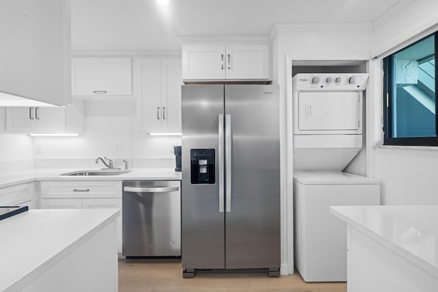 kitchen featuring stacked washer / dryer, light wood-type flooring, appliances with stainless steel finishes, white cabinets, and sink