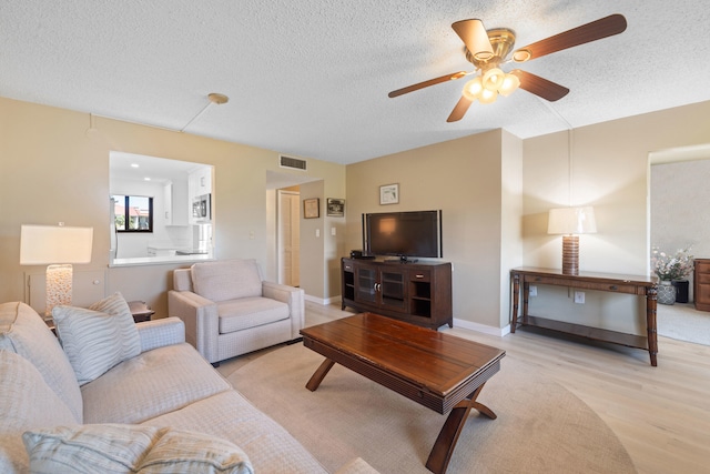 living room with ceiling fan, light hardwood / wood-style floors, and a textured ceiling