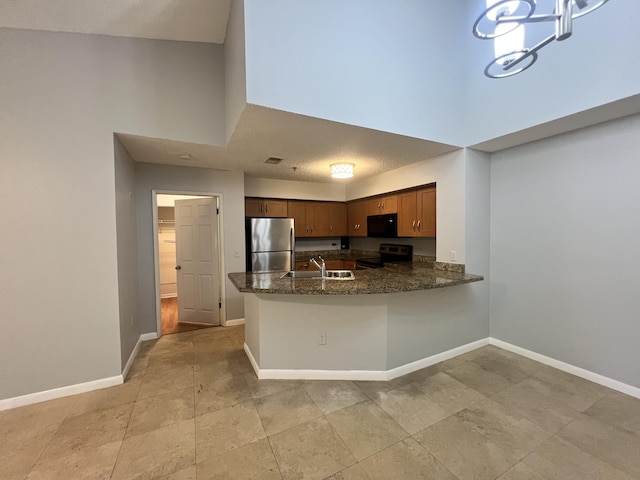 kitchen with sink, a high ceiling, a notable chandelier, kitchen peninsula, and appliances with stainless steel finishes