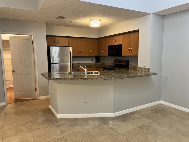 kitchen featuring dark stone counters, sink, a textured ceiling, kitchen peninsula, and stainless steel appliances