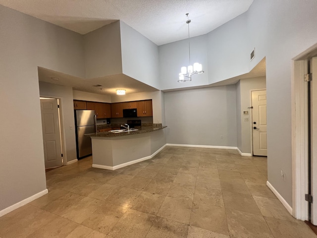 kitchen featuring sink, an inviting chandelier, kitchen peninsula, stainless steel fridge, and a towering ceiling