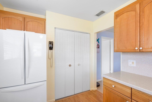 kitchen featuring white refrigerator, light hardwood / wood-style floors, and decorative backsplash