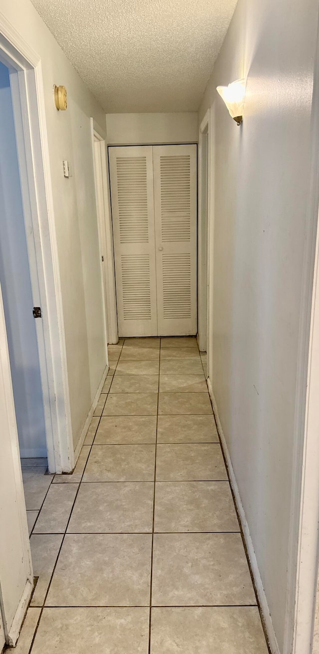 hallway with a textured ceiling and light tile patterned floors