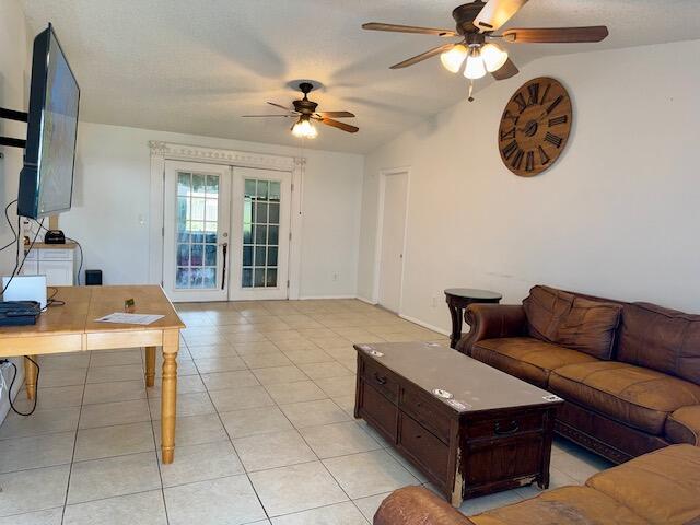 tiled living room featuring french doors, ceiling fan, and vaulted ceiling