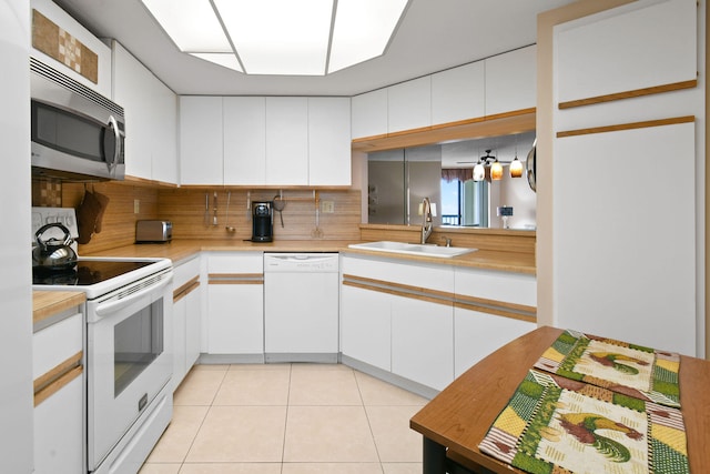 kitchen with tasteful backsplash, white appliances, light tile flooring, sink, and white cabinets