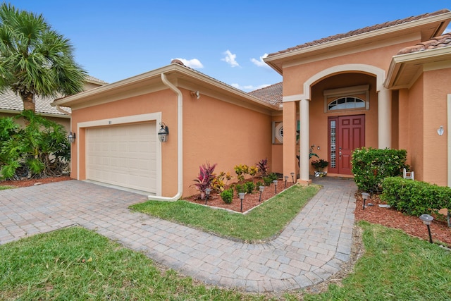 entrance to property with a garage, a tiled roof, and stucco siding