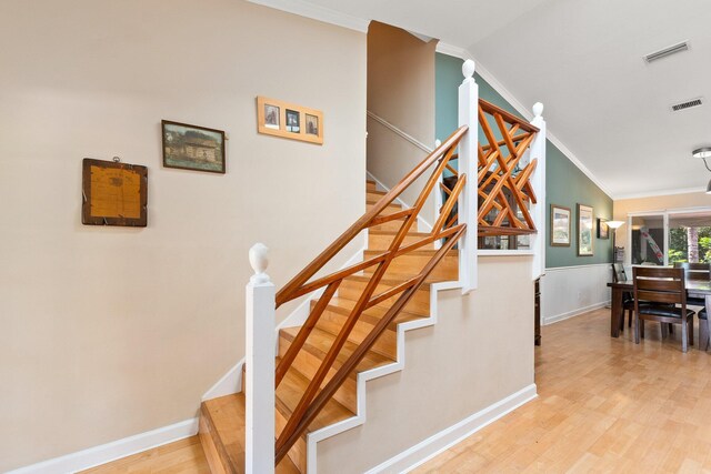 stairway with ornamental molding, light wood-type flooring, and vaulted ceiling