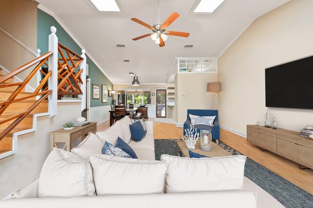 living room featuring ornamental molding, ceiling fan, light wood-type flooring, and vaulted ceiling with skylight