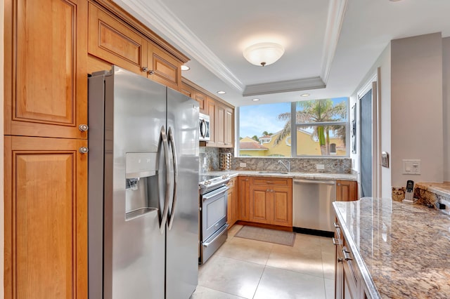 kitchen with light stone counters, a raised ceiling, ornamental molding, light tile patterned flooring, and appliances with stainless steel finishes