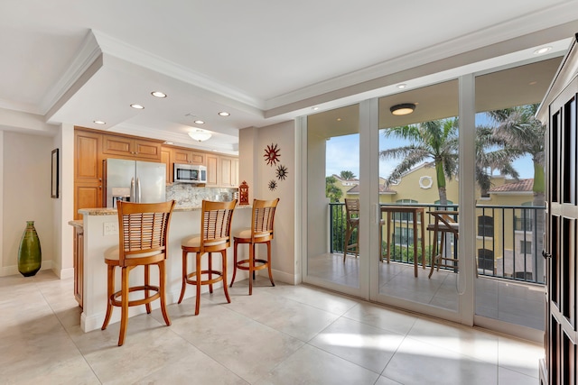 kitchen with ornamental molding, appliances with stainless steel finishes, light stone countertops, a kitchen bar, and decorative backsplash