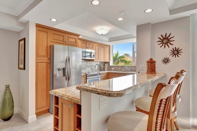 kitchen featuring light stone counters, kitchen peninsula, stainless steel appliances, a kitchen breakfast bar, and decorative backsplash