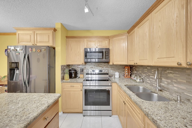 kitchen featuring light stone counters, light brown cabinets, a sink, appliances with stainless steel finishes, and tasteful backsplash