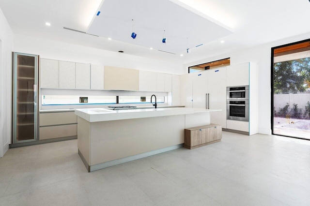 kitchen with stainless steel double oven, white cabinets, sink, and a spacious island