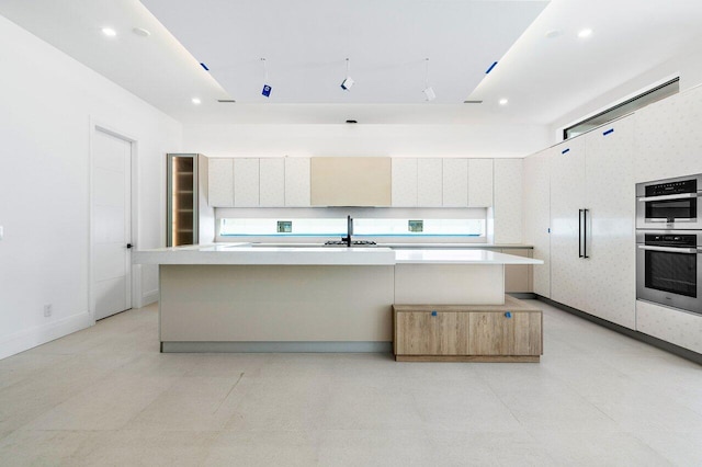 kitchen featuring an island with sink, sink, white cabinets, and double oven