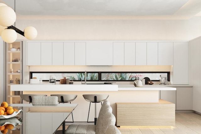 kitchen with light hardwood / wood-style flooring, white cabinets, a kitchen breakfast bar, and decorative light fixtures