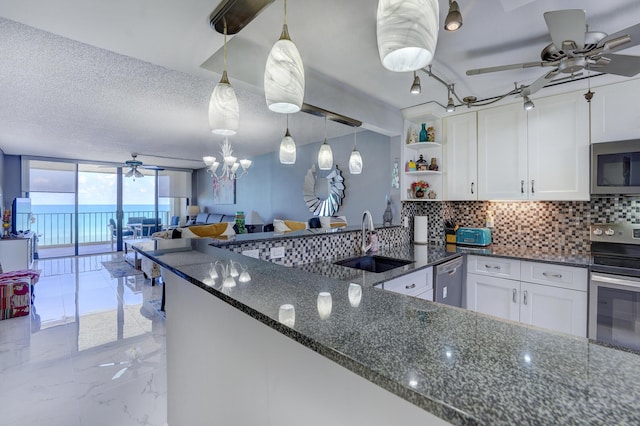 kitchen with dark stone counters, stainless steel appliances, sink, pendant lighting, and white cabinetry