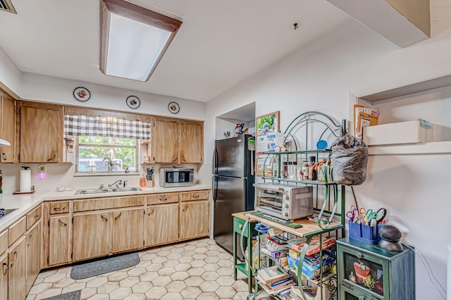 kitchen featuring sink, light tile flooring, and black refrigerator