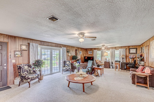 carpeted living room with french doors, wooden walls, ceiling fan, and a textured ceiling