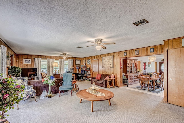 carpeted living room featuring wood walls, ceiling fan, and a textured ceiling