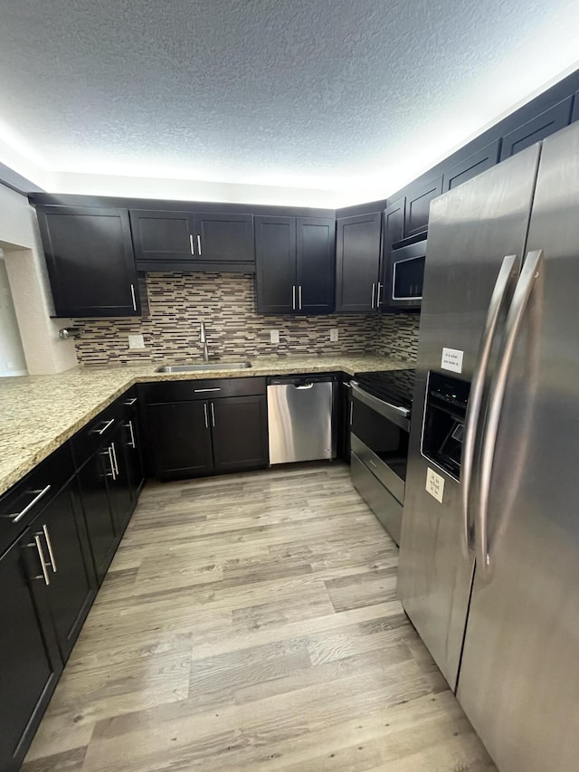 kitchen featuring sink, stainless steel appliances, light stone counters, tasteful backsplash, and light hardwood / wood-style floors