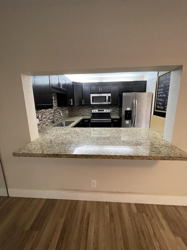 kitchen featuring sink, hardwood / wood-style flooring, appliances with stainless steel finishes, light stone countertops, and kitchen peninsula