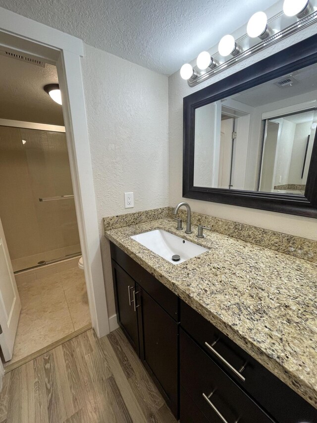 bathroom with walk in shower, toilet, wood-type flooring, a textured ceiling, and vanity