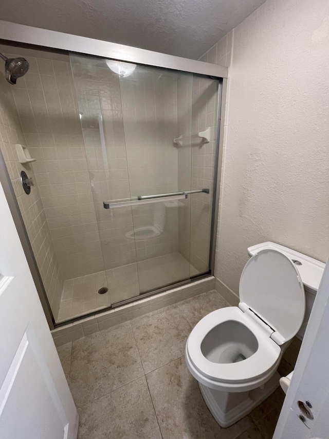 bathroom featuring toilet, an enclosed shower, tile patterned flooring, and a textured ceiling