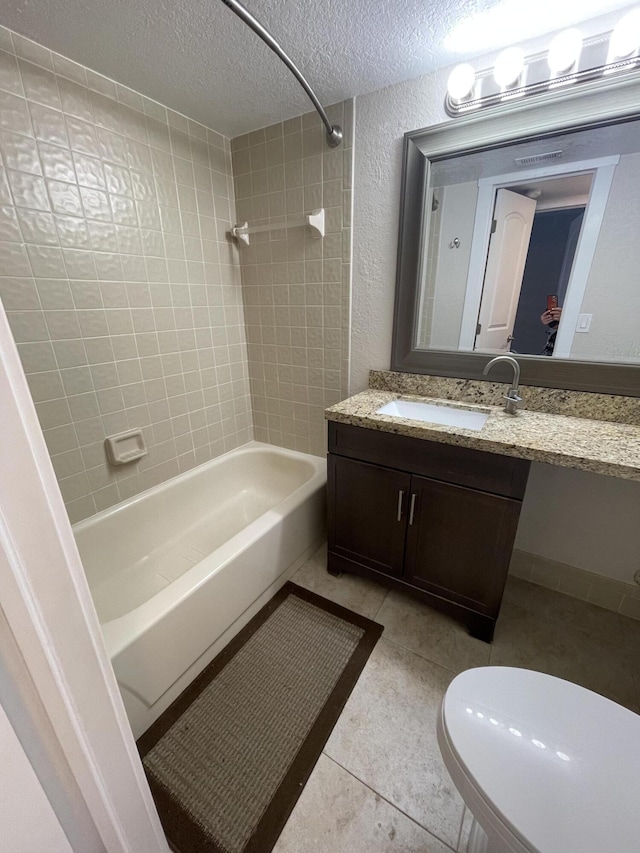 full bathroom featuring toilet, a textured ceiling, vanity, tiled shower / bath combo, and tile patterned flooring