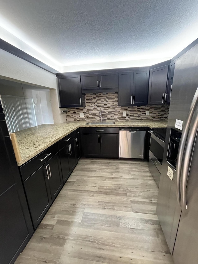 kitchen featuring stainless steel appliances, light stone countertops, sink, and light hardwood / wood-style flooring