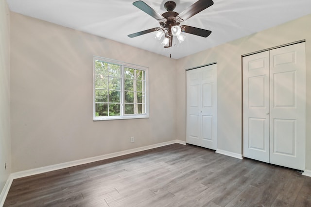 unfurnished bedroom featuring ceiling fan, multiple closets, and hardwood / wood-style floors