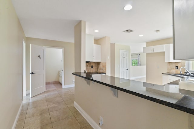 kitchen featuring white cabinets, dark stone countertops, sink, kitchen peninsula, and light tile patterned flooring