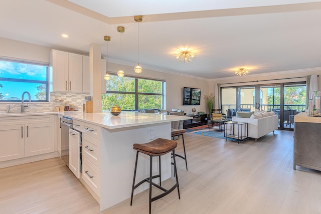 kitchen featuring pendant lighting, sink, a breakfast bar area, white cabinets, and backsplash