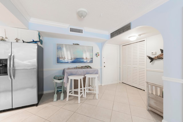 kitchen with stainless steel refrigerator with ice dispenser, ornamental molding, a textured ceiling, and light tile floors