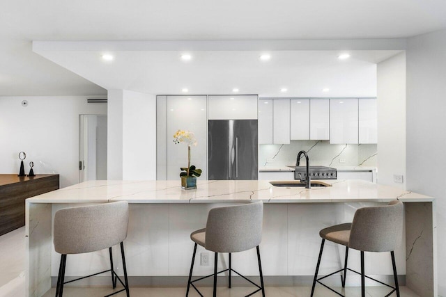 kitchen with white cabinetry, sink, tasteful backsplash, and stainless steel fridge