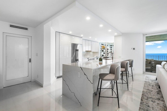 kitchen with stainless steel fridge, light tile flooring, backsplash, a breakfast bar, and white cabinets