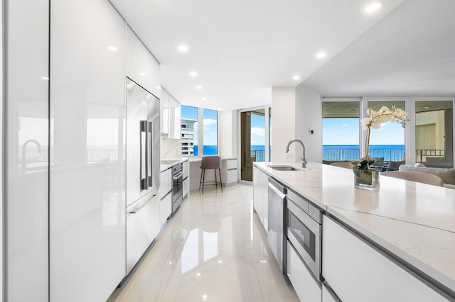 kitchen with expansive windows, light stone counters, light tile floors, sink, and white cabinetry