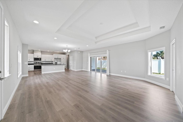 unfurnished living room featuring light hardwood / wood-style floors, an inviting chandelier, and a tray ceiling