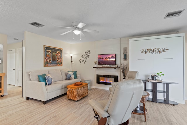 living room with ceiling fan, a large fireplace, a textured ceiling, and hardwood / wood-style floors