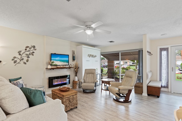 living room featuring ceiling fan, a textured ceiling, and light hardwood / wood-style flooring