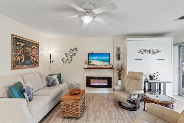 living room featuring ceiling fan, a fireplace, a textured ceiling, and hardwood / wood-style floors