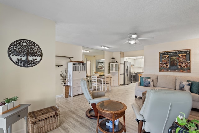 living room with a textured ceiling, ceiling fan, and light hardwood / wood-style flooring