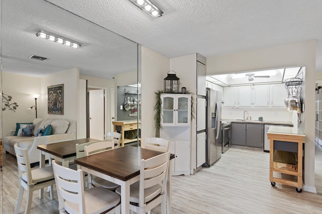 dining space featuring ceiling fan, sink, a textured ceiling, and light hardwood / wood-style flooring