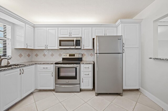 kitchen featuring appliances with stainless steel finishes, dark stone counters, sink, light tile patterned floors, and white cabinets