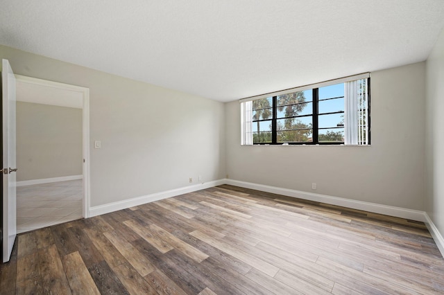 empty room with a textured ceiling and light hardwood / wood-style flooring