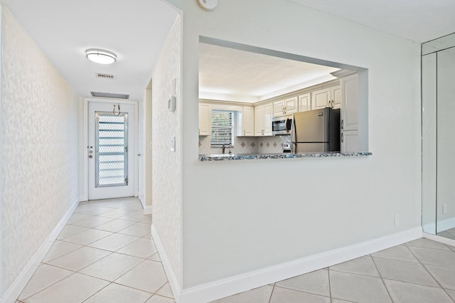 kitchen with light tile patterned floors, tasteful backsplash, cream cabinetry, stone countertops, and stainless steel appliances