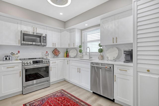 kitchen with appliances with stainless steel finishes, light wood-type flooring, tasteful backsplash, sink, and white cabinetry